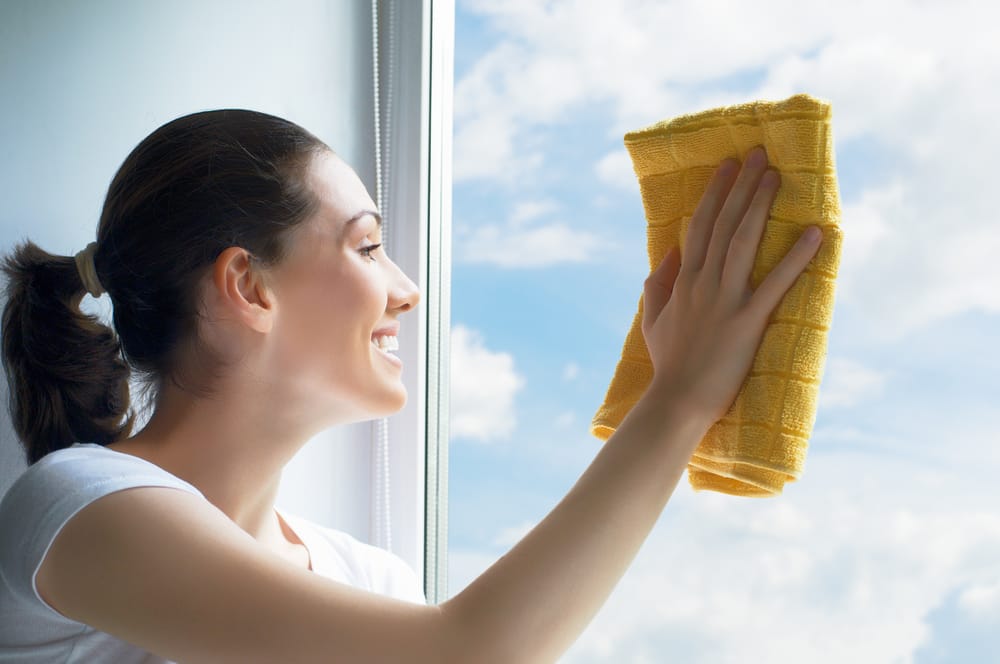 Une femme qui nettoie une vitre avec un chiffon jaune
